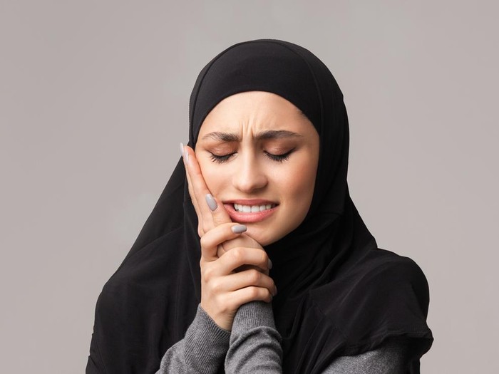 Aching tooth. Unhappy arabic woman in hijab suffering from teeth pain, having caries, touching her cheek with miserable face expression, panorama