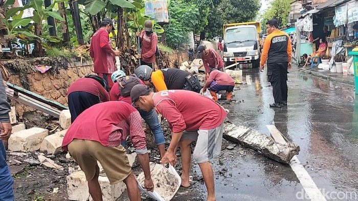 Petugas membersihkan material tembok sungai ambrol