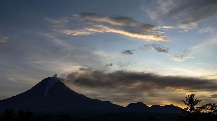 A man rides a motorcycle past a river, while Mount Merapi, a volcanic mountain spews volcanic material in South Kaliurang village, Srumbung district in Central Java, Indonesia on April 30, 2023. Merapi is located in one of the most densely populated parts of Java with over 11,000 people living on the slopes of the mountain. Mount Merapi, measuring 2,968 metres high, is known as one of the most active volcanoes in Indonesia, with an eruption occurring every two to five years. (Photo by Garry Lotulung/NurPhoto via Getty Images)