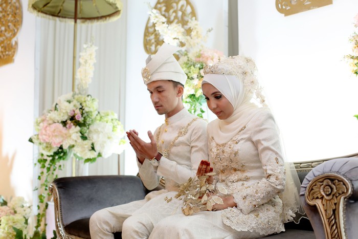 A pair of newlywed Muslim bride and groom seated for prayers at pelamin (a decorated newlywed seating at the main stage) in wedding reception, Kuala Lumpur Malaysia.