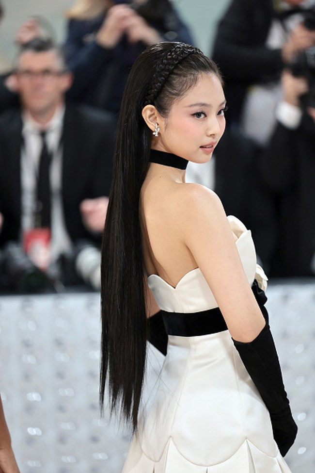 Gaun bustier satin yang dikenakannya memiliki aksen pita berhias kamelia putih. Bunga yang sama disematkan pada rambutnya. Jennie pun memakai sarung tangan hitam, stocking, dan heels serasi untuk melengkapi penampilannya. Foto: Getty Images