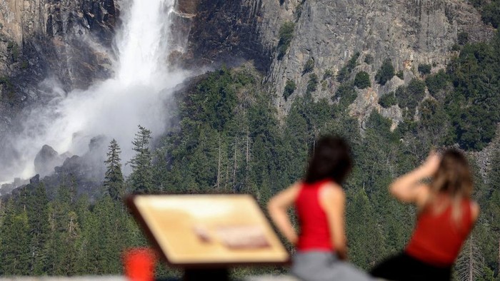 Potret Indahnya Air Terjun di Taman Nasional Yosemite yang 'Mengancam' YOSEMITE NATIONAL PARK, CALIFORNIA - APRIL 28: People take photos as water flows forcefully down Lower Yosemite Fall in Yosemite Valley, as warming temperatures have increased snowpack runoff, on April 28, 2023 in Yosemite National Park, California. Most of Yosemite Valley will close this evening until May 3rd because of forecasted flooding from melting snowpack and extended high temperatures. Yosemite Falls is fed almost completely by snowmelt and is the tallest waterfall in North America when measured from the peak of the upper fall to the base of the lower fall. As of April 1, snowpack in the Tuolumne River basin of Yosemite National Park was 244% of average amid record snowpack levels for some parts of California after years of drought. (Photo by Mario Tama/Getty Images)