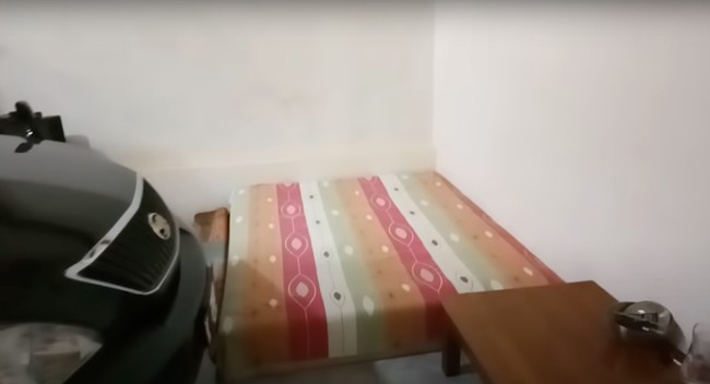 Masuk ke bagian dalam rumah, terdapat sebuah ruangan yang bisa dijadikan sebagai kamar tidur sekaligus garasi. Terlihat sebuah mobil hitam yang terparkir di dalam rumah tersebut. Berbeda dari dapur, ruangan ini sudah memiliki lantai yang dikeramik. Foto: YouTube/Kromo Chanel