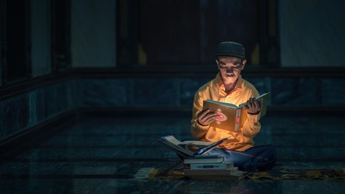 Ilustrasi seorang muslim sedang membaca Al-Quran sebelum tidur.