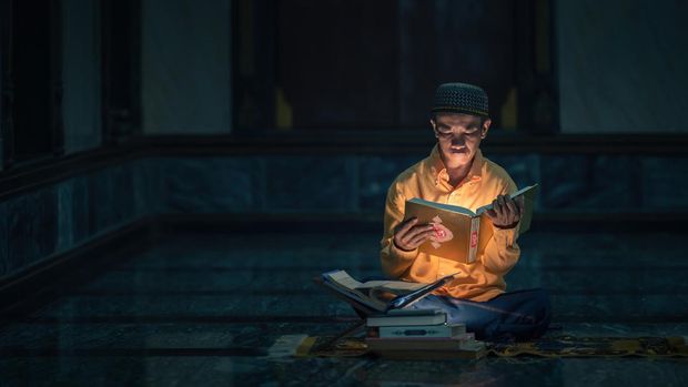 Ilustrasi seorang muslim sedang membaca Al-Qur'an sebelum tidur.