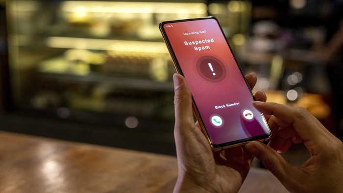 A woman receiving an incoming suspected spam call on her phone. The network provider detect the scam and show warning sign, woman rejects the call.