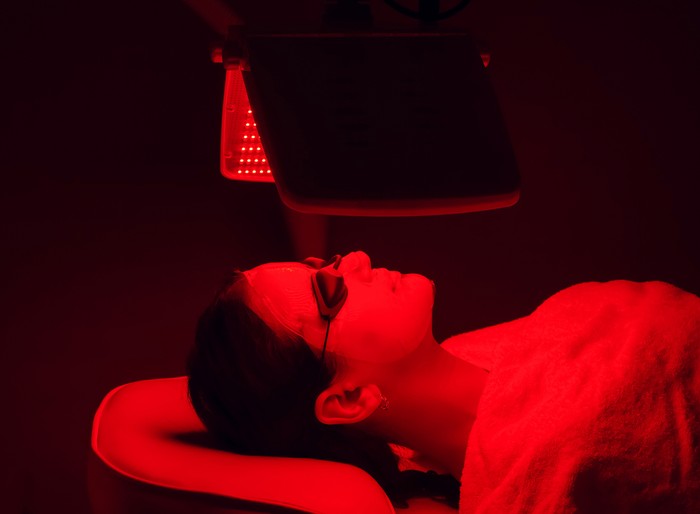 Young woman having red LED light facial therapy treatment in beauty salon. Beauty and wellness concept