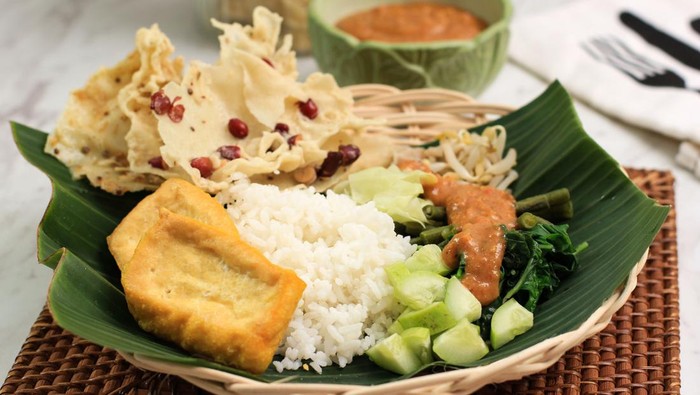 Nasi Pecel. Traditional Javanese Rice Dish of Steamed Rice with Vegetable Salad, Peanut Sauce Dressing, Tempeh, Tofu Beancurd, and Peyek Crackers. Pecel Madiun is Most Popular Variant