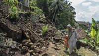 Warga melintas di jalan yang tertimbun material longsor di Desa Banyurasa, Kabupaten Tasikmalaya, Jawa Barat. 