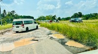 Jalanan tersebut tampak tidak beraspal dan banyak lubang di berbagai sisinya. Beberapa lubang bahkan terlihat tergenang air. 