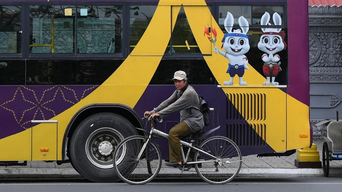 Semarak SEA Games 2023 di Kamboja A man rides his bicycle in front of a bus with the mascots and logo of the 32nd Southeast Asian Games (SEA Games) in Phnom Penh on May 4, 2023. (Photo by Nhac NGUYEN / AFP) (Photo by NHAC NGUYEN/AFP via Getty Images)