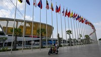 Orang-orang mengendarai skuter di depan bendera di Stadion Nasional Morodok Techo menjelang Pesta Olahraga Asia Tenggara (SEA Games) ke-32. Pembukaan akan digelar di Stadion Morodok Techo, Phnom Penh. Opening ceremony ini akan dimulai sekitar sore hari. Nantinya pembukaan kejuaraan ini akan diisi oleh pawai kontingen sebelum nantinya turnamen ini akan dibuka oleh kepala negara Kamboja, Perdana Menteri Hun Sen. Mohd Rasfan/AFP/Getty Images  