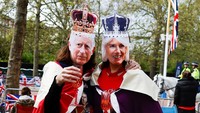 Dua orang warga menyaksikan prosesi penobatan dengan memakai topeng Raja Charles dan Ratu Camilla yang memakai mahkota. Reuters/Clodagh Kilcoyne.