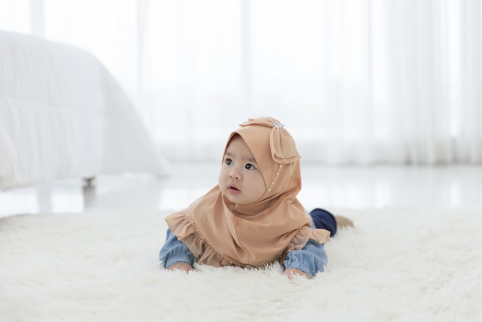 Baby girl 6 months crawling on the floor in the bedroom.  Children Asian in hijab clothing