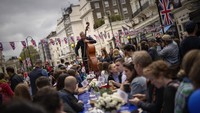 Seorang musisi memainkan double bassnya saat orang-orang duduk di meja panjang untuk menyantap makan siang mereka sebagai bagian dari perayaan Makan Siang Besar di London. Makan Siang Besar adalah bagian dari perayaan akhir pekan Penobatan Raja Charles III. AP/Emilio Morenatti  