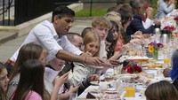 Perdana Menteri Rishi Sunak menyerahkan sepotong kue kepada seorang tamu saat ia menghadiri pesta Makan Siang Besar di Downing Street di London. Para tamu pada jamuan makan siang itu termasuk para pahlawan komunitas dan orang-orang Ukraina yang terlantar akibat perang, dan kelompok-kelompok pemuda. AP/Frank Augstein  