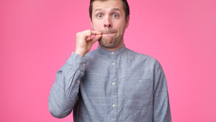 Young man showing a sign of closing mouth and silence gesture doing like closing his mouth with a zipper on isolated pink background