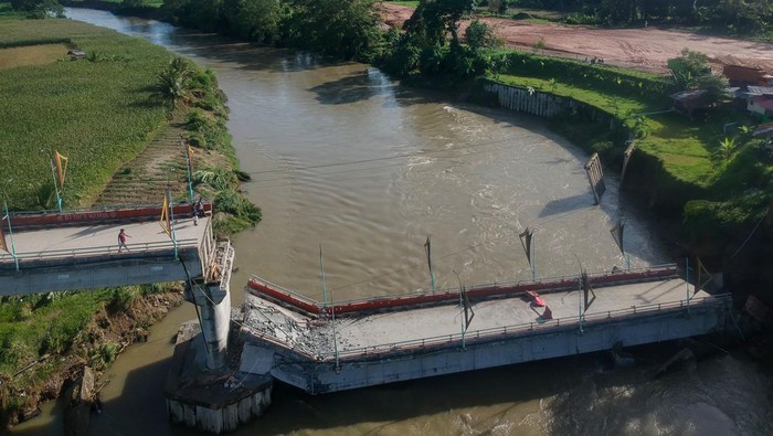 Jembatan Bantuan BNPB di Sumbar Senilai Rp 25,4 M Ambruk Foto udara warga melihat kondisi jembatan ambruk di Kayu Gadang Sikabu, Lubuk Alung, Padang Pariaman, Sumatera Barat, Senin (8/5/2023). Jembatan terpanjang di kabupaten itu yang dibangun dari dana hibah Badan Nasional Penanggulangan Bencana (BNPB) senilai Rp25,4 miiar dan baru diresmikan pada Agustus 2021 tersebut, ambruk pada Senin (8/5/2023) malam pascameluapnya Sungai Batang Anai. ANTARA FOTO/Iggoy el Fitra