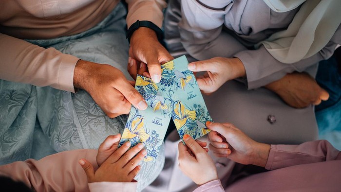 A family wearing a Baju Melayu and Sampin Songket holding a pocket money envelope for muslim Eid celebration or also known as 