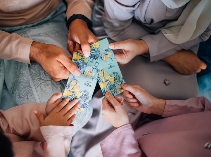 A family wearing a Baju Melayu and Sampin Songket holding a pocket money envelope for muslim Eid celebration or also known as 