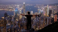Seorang turis berfoto dengan latar kawasan pusat keuangan dan Pelabuhan Victoria Hong Kong.