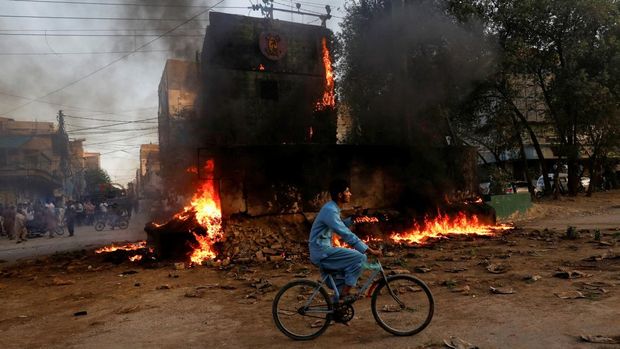 Seorang anak laki-laki melewati pos pemeriksaan paramiliter, yang dibakar oleh para pendukung mantan Perdana Menteri Pakistan Imran Khan, selama protes terhadap penangkapannya di Karachi, Pakistan, Selasa (9/5/2023). (REUTERS/AKHTAR SOOMRO)