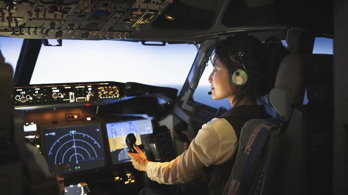 Rear view of a female pilot sitting the cockpit of a flight. Woman pilot flying an airplane.