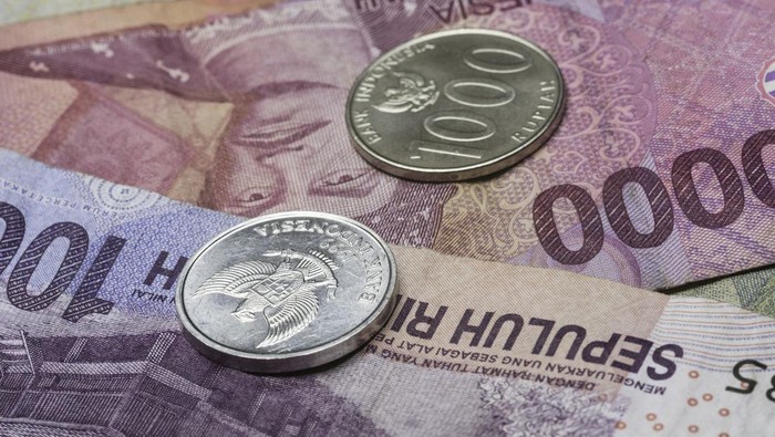 Macro close-up of Indonesian 100 and 1000 Rupiah coins on top of Indonesian banknotes.