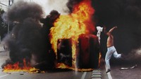 Seorang pemuda melempar kainnya ke mobil yang terbakar di jalan Otista, Jakarta Timur, ketika massa tertahan di sekitar Jakarta, Kamis (14/5/1998). Kerusuhan massa telah terjadi setelah empat mahasiswa Universitas Trisakti ditembak mati oleh polisi anti huru hara sementara para mahasiswa mengadakan demonstrasi massa menyerukan agar Soeharto mengundurkan diri.  ANTARA FOTO/Zarqoni Maksum 