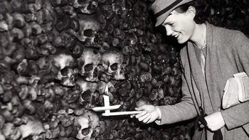 Seorang pengunjung dengan lilin di tangannya tersenyum melihat banyaknya koleksi tengkorak di katakombe Paris. 1935. Foto: Rarehistoricalphotos