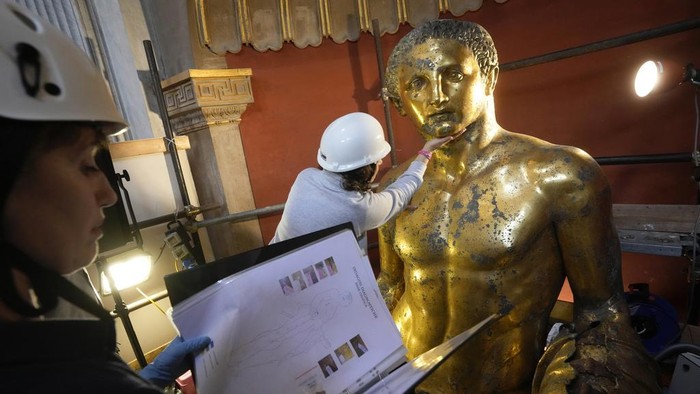 Wujud Patung Hercules Raksasa yang Ditemukan di Museum Vatikan Vatican Museum restorers Chiara Omodei Zorini, left, and Alice Baltera work on the bronze Hercules statue, in the Round Hall of the Vatican Museums, Thursday, May 11, 2023. Work will continue until December to reveal the 4-meter- (13-foot-) tall Hercules, believed to have stood in ancient Romeβs Pompey Theater, to its original golden sheen. The discovery of the gilded bronze in 1864 during work on a bankerβs villa near Piazza dei Fiori made global headlines. (AP Photo/Andrew Medichini)