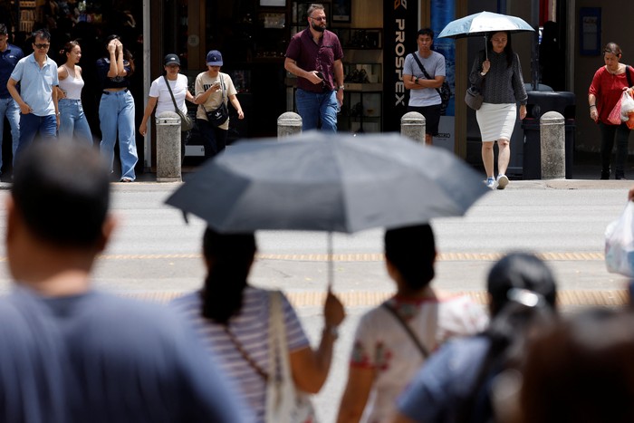 People shield themselves from the sun with umbrellas as they cross a street on a warm day in Singapore May 15, 2023. REUTERS/Edgar Su