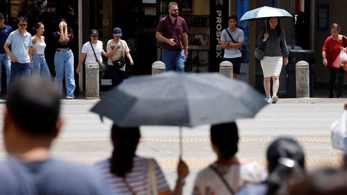 People shield themselves from the sun with umbrellas as they cross a street on a warm day in Singapore May 15, 2023. REUTERS/Edgar Su