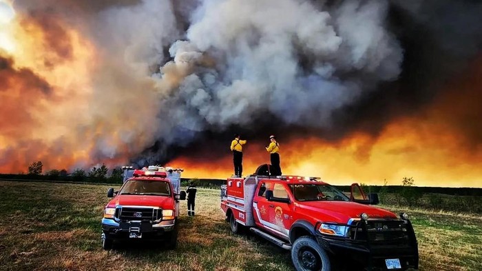Kota di Kanada Berselimut Asap Kuning Imbas Kebakaran Hutan Firefighters stand on a Kamloops Fire Rescue truck at a wildfire near Fort St. John, British Columbia, Canada May 14, 2023. Kamloops Fire Rescue/Handout via REUTERS THIS IMAGE HAS BEEN SUPPLIED BY A THIRD PARTY. NO RESALES. NO ARCHIVES