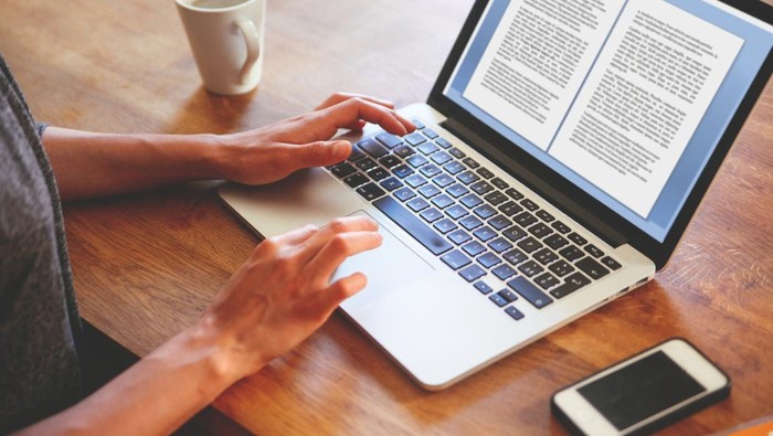 High angle image of a female novelist or blogger, typing on the laptop keyboard while having a cup of coffee. Retro processed with vibrant colors.