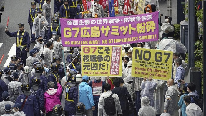 Police officers walk beside protesters chanting against the Group of Seven (G7) nations' meetings as they march on a street in Hiroshima, western Japan, Friday, May 19, 2023. (Kyodo News via AP)