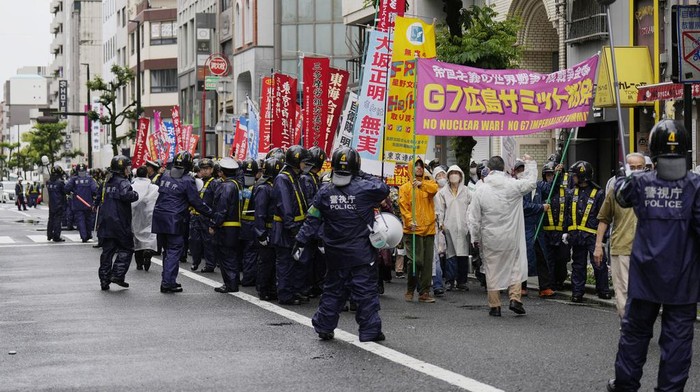 Police officers walk beside protesters chanting against the Group of Seven nations' meetings as they march on a street in Hiroshima, western Japan, Friday, May 19, 2023. The G7 summit starts Friday. (AP Photo/Hiro Komae)