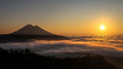 The sun shines through trees during sunrise in Kintamani, Bali, Indonesia, on May 18, 2023. (Photo by Garry Lotulung/NurPhoto via Getty Images)