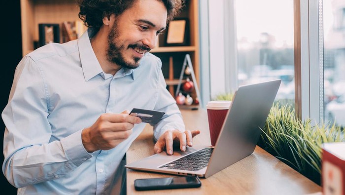 Man making an online payment via credit card on a laptop at an internet cafe.