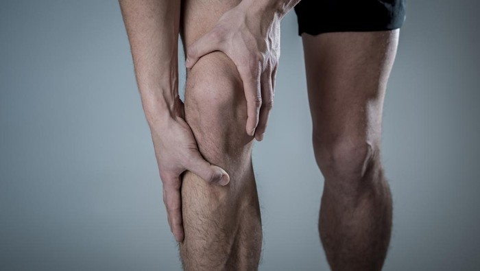 Young fit man holding knee with hands in pain after suffering muscle injury broken bone leg pain sprain or cramp during running workout. In Body pain and sport training injury and body health care.