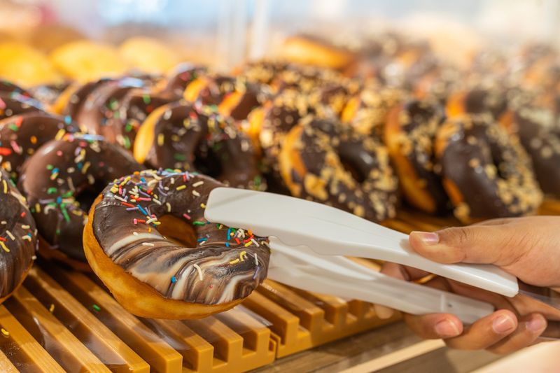 Woman hand using clamp picking yummy chocolate donut at pastry shop