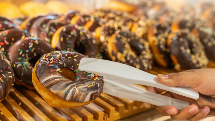 Woman hand using clamp picking yummy chocolate donut at pastry shop