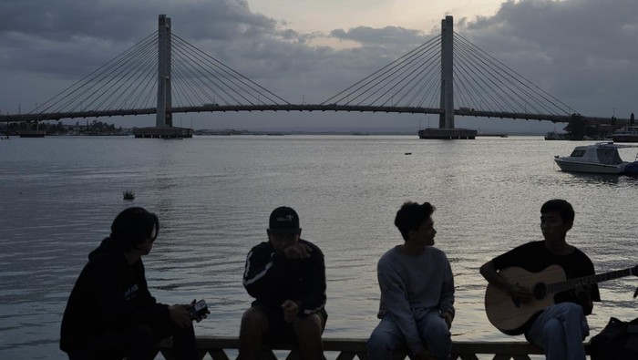 Sejumlah warga duduk dengan latar belakanbg Jembatan Teluk Kendari di Kendari, Selasa (23/5/2023). Pembangunan Jembatan Teluk Kendari sepanjang 1.380 meter tersebut memberikan dampak positif seperti kelancaran lalu lintas dan memicu tumbuhnya aktivitas perekonomian antara kabupaten-kabupaten yang menghubungkan ke pusat Kota Kendari sehingga berdampak pada pertumbuhan produk domestik regional bruto. ANTARA FOTO/Jojon/tom.