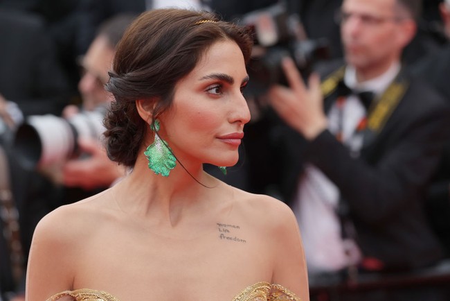 Namun yang membuat penampilannya mencuri perhatian bukan karena busananya. Melainkan tato di bahunya yang bertuliskan Women, Life, Freedom. Foto: Getty Images