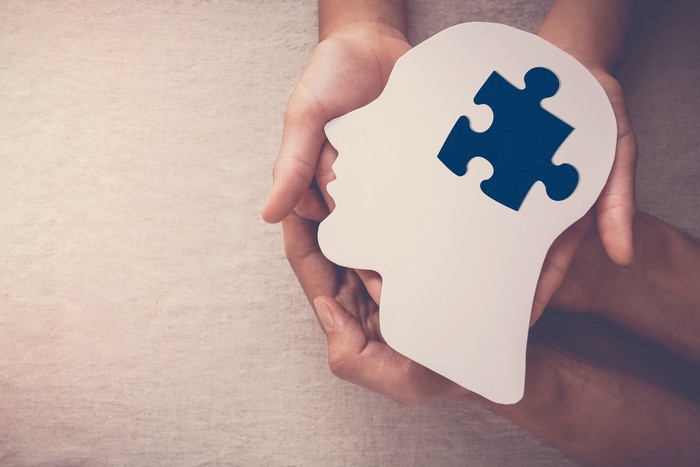 hands holding puzzle piece missing in brain paper cutout, autism, dementia, mental health concept