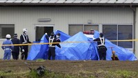 Petugas polisi menutupi kendaraan polisi yang diparkir di depan sebuah gedung dekat sebuah rumah tempat seorang pria bersembunyi di Nakano. Sebelumnya, tiga orang tewas dalam peristiwa penembakan dan penusukan di Jepang bagian tengah, Nagano.