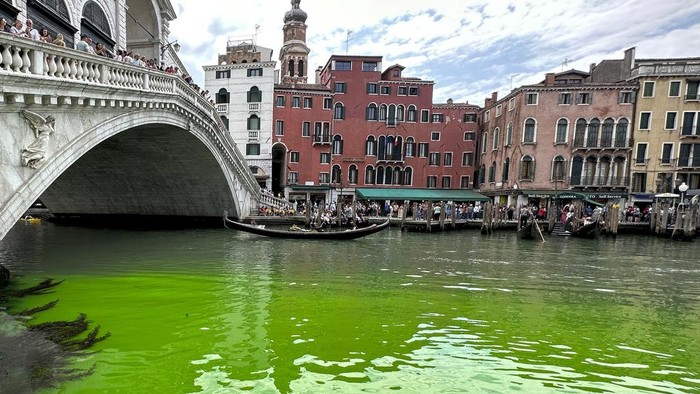 Gondolas navigate by the Rialto Bridge on Venice's historical Grand Canal as a patch of phosphorescent green liquid spreads in it, Sunday, May 28, 2023. The governor of the Veneto region, Luca Zaia, said that officials had requested the police to investigate to determine who was responsible, as environmental authorities were also testing the water. (AP Photo/Luigi Costantini)