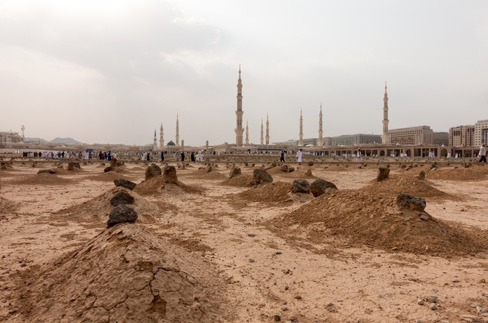Ancient graves in Jannat Al Baqi Cemetery and the Prophets Mosque al Masjid an Nabawi at the background in Medina, Saudi Arabia