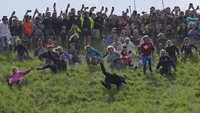 Peserta berkompetisi dalam lomba lari menuruni bukit dalam kontes Cheese Rolling di Coopers Hill, Brockworth, Gloucestershire, Inggris, Senin (29/5/2023).  
