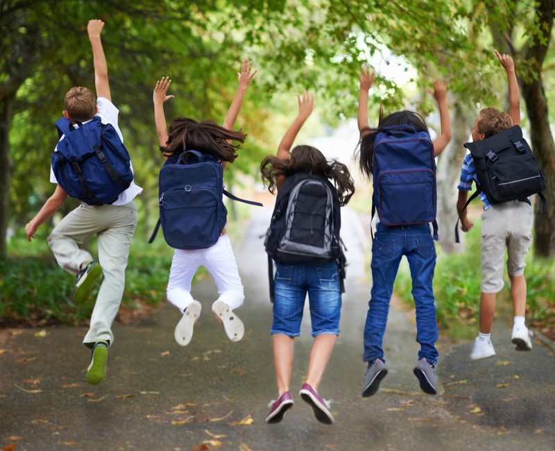 Rear-view of five children jumping in the air wearing backpacks